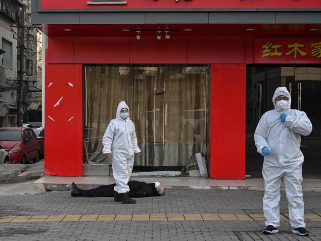 Officials in protective suits check on an elderly man wearing a facemask who collapsed and died on a street near a hospital in Wuhan. Picture: AFP