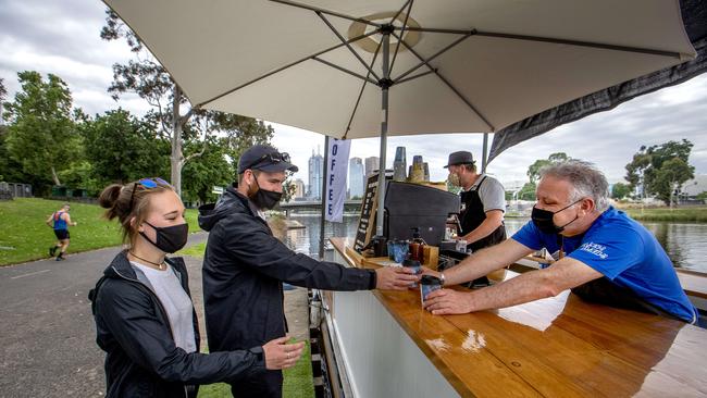 A couple wearing masks buy coffee from a floating cafe on the Yarra river on Sunday morning as restrictions on mandatary mask wearing are eased in Melbourne from midnight. Picture: NCA NewsWire / David Geraghty