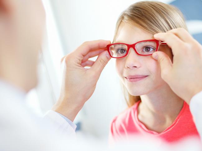 Little brown eyed  girl visiting optician.She's having appointment for testing new glasses.Middle aged male optician is gently adjusting new frame and glasses on girl's face. Picture: iStock