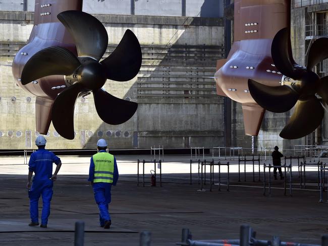 Technicians walk near a propeller of the ship.