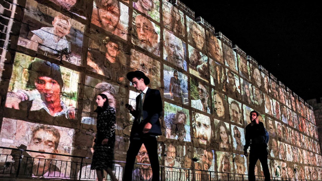 People walk outside the walls of the old city of Jerusalem, on which are projected pictures of the hostages abducted by Palestinian militants in the October 7 attack and are held in the Gaza Strip. Picture: Ahmad Gharabli/AFP