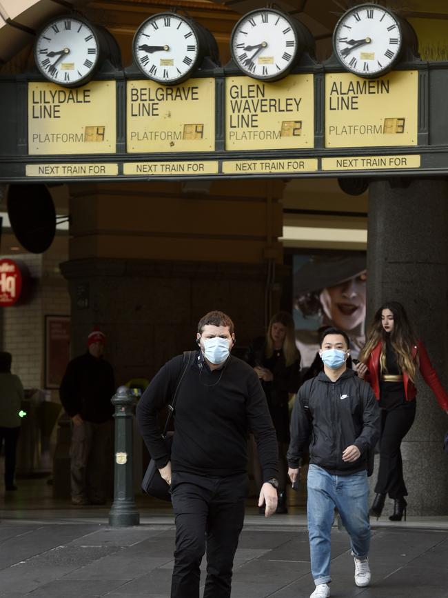 Commuters wearing masks exit Flinders Street Station.