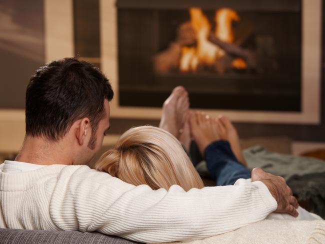 Young couple hugging on sofa in front of fireplace at home, rear view. Click here for more 