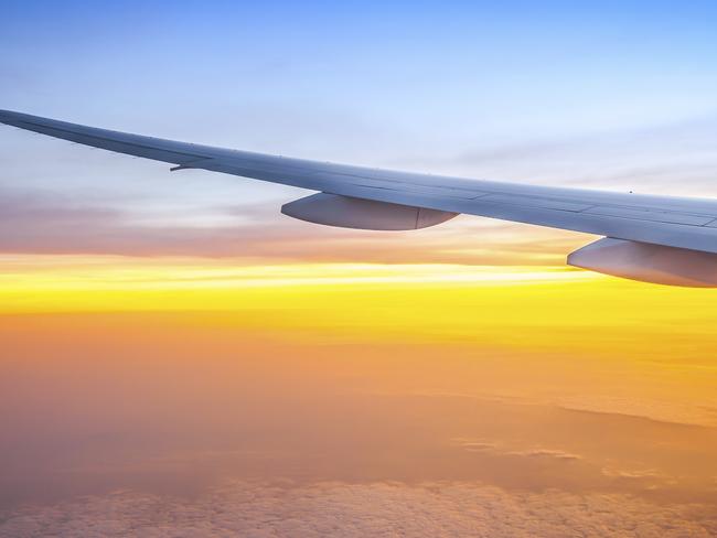 Airplane wing and sunrise over clouds