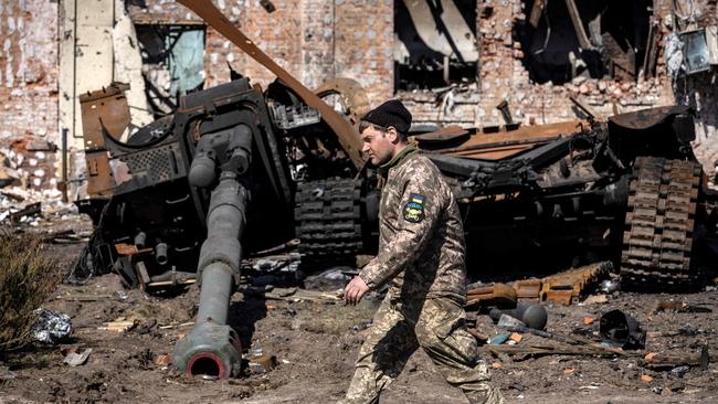 A Ukrainian serviceman walks between damaged Russian army tank and rubble of a destroyed building in the northeastern city of Trostianets.