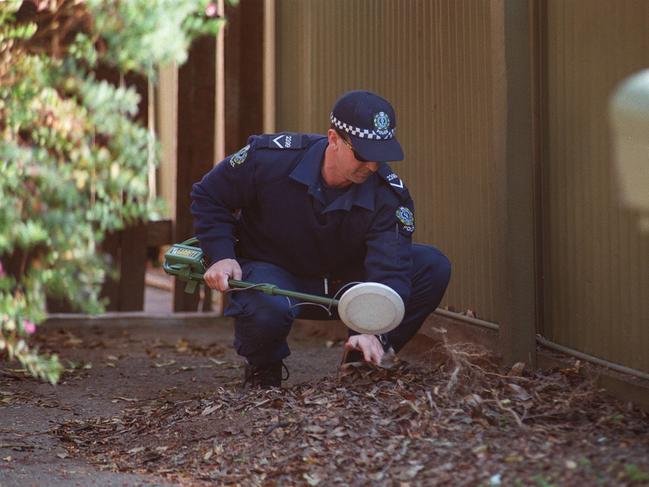 Police examine the grounds outside the unit of Corinna Marr, who was murdered inside in 1997. Her murder has not been solved.