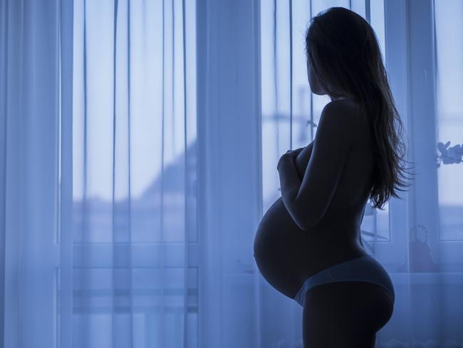 Beautiful pregnant woman looking out the window, silhouette