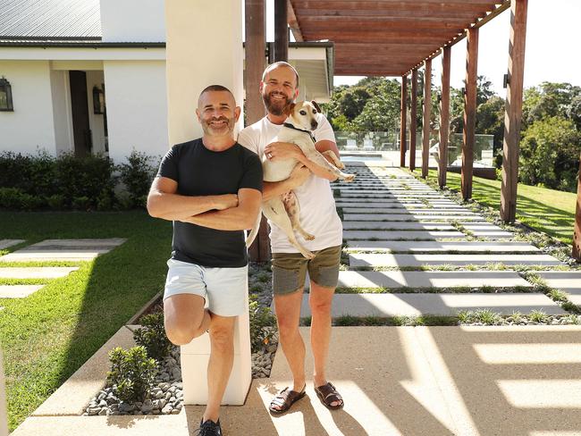 18/9/2019 : Interior designers Gavin Atkins and  Warren Sonin (in white T) holding Charlie the dog  (Gav and Waz), at their home at Cooroy on the Sunshine Coast. The pair were on the first series of reality renovation show The Block in 2003 and have transformed their Cooroy Mountain property into a luxury lodge. Lyndon Mechielsen/The Australian