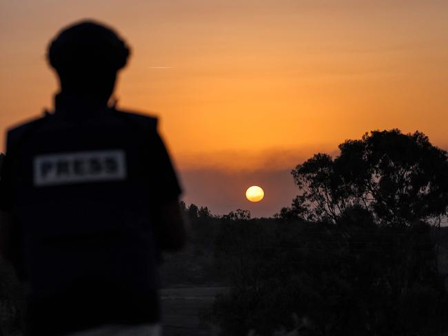 A journalist looks on as the sun sets over the Gaza Strip off a position across the border in southern Israel on November 8, 2023 amid ongoing battles between Israel and the Palestinian Hamas movement. (Photo by Jack Guez / AFP)