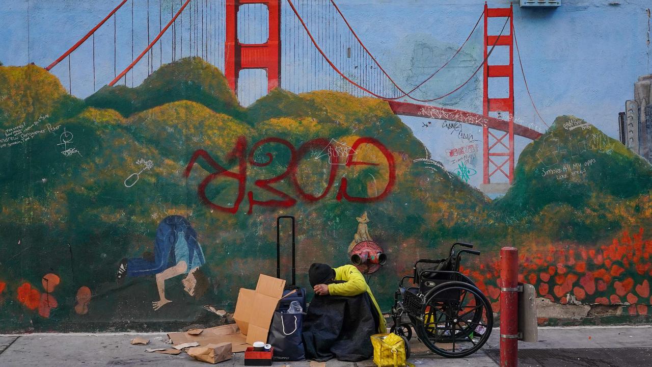 A homeless person lies against a mural near APEC Summit headquarters. Picture: Loren Elliott / AFP