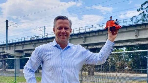 Councillor Cameron Caldwell holding up a toy train at the future site of the station site.