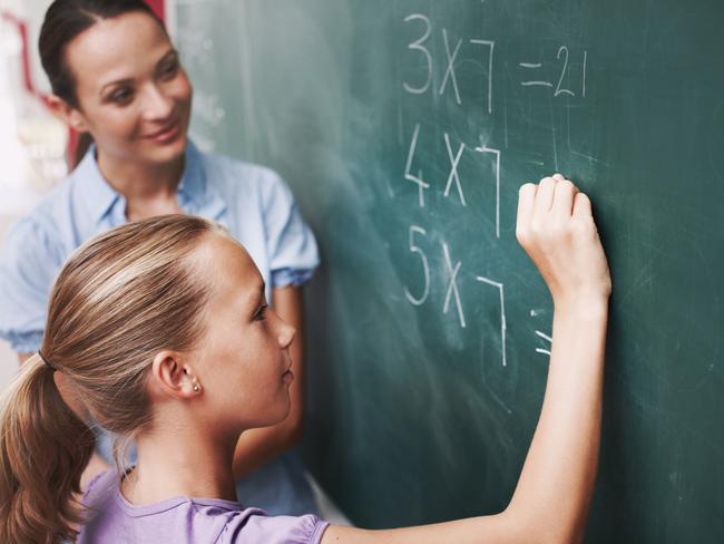 EDUCATION:  A young girl doing maths on the board as her teacher watches smiling