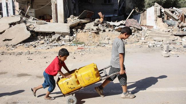 Palestinian boys transport water containers past buildings destroyed during a previous Israeli bombardment in Gaza City on Monday. Picture: Omar Al-Qattaa / AFP