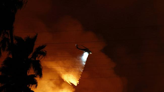 LOS ANGELES, CALIFORNIA - JANUARY 10: A firefighting helicopter drops water as the Palisades Fire burns toward the Mandeville Canyon neighborhood on January 10, 2025 in Los Angeles, California. Multiple wildfires fueled by intense Santa Ana Winds are burning across Los Angeles County. Reportedly at least 10 people have died with over 180,000 people having been under evacuation orders. Over 9,000 structures have been damaged or burned while more than more than 25,000 acres were burning from the fires.   Mario Tama/Getty Images/AFP (Photo by MARIO TAMA / GETTY IMAGES NORTH AMERICA / Getty Images via AFP)