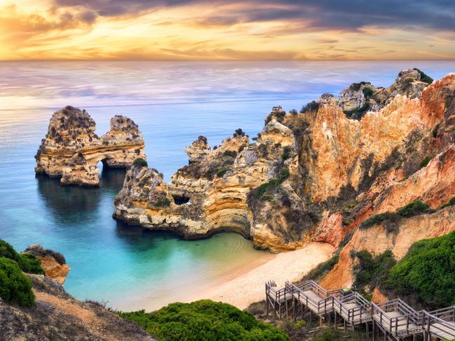 The beautiful Camilo Beach in Lagos, Portugal, with its magnificent cliffs and the blue ocean colorfully lit at sunrise