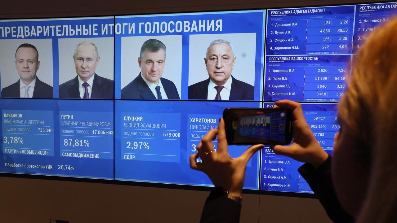 A woman takes a photograph of a screen with early voting results in the Russian presidential election. Picture: Stringer / AFP