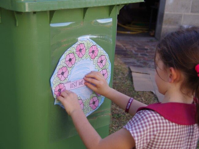 Grace and her grandfather Garry stuck Anzac Day posters to the wheelie bin. Photo: Contributed