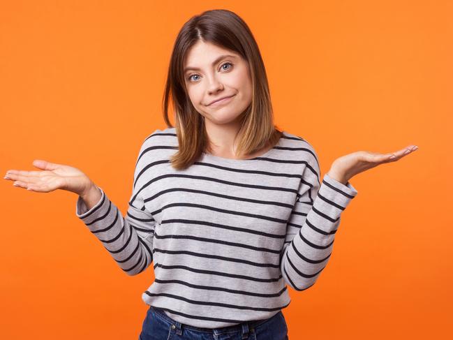 Don't know! Portrait of uncertain confused brunette woman in long sleeve shirt standing having doubts while raised hands, clueless facial expression. indoor studio shot isolated on orange background