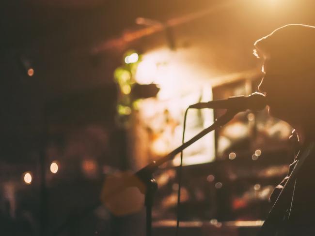 A male singer on a stage performing with guitar at a bar generic, music, microphone, shadow. Picture: iStock