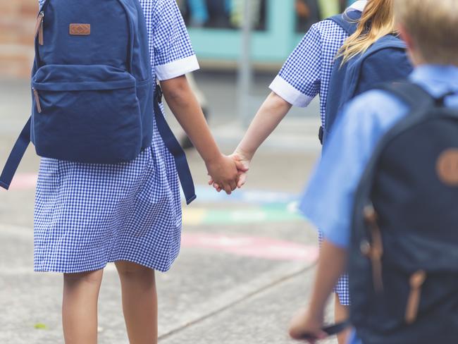 School children walking away. They are wearing uniforms and carrying backpacks. They are having a race. Multi ethnic group with Caucasian and Aboriginal children. Rear view. girls are holding hands