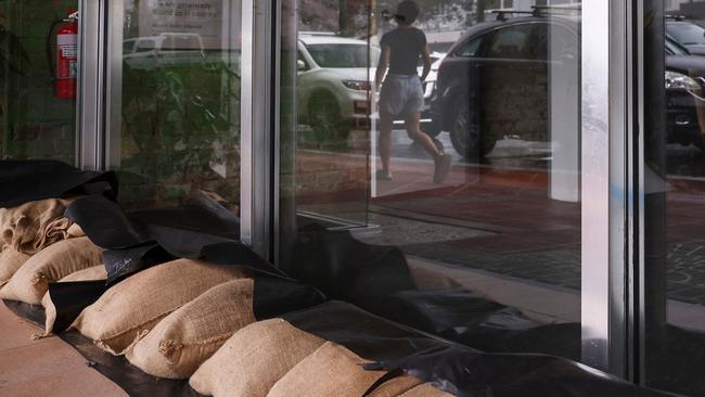 A resident is reflected in a window as she walks past a row of sandbags covering the front of a shop in the town of Lismore on March 5, 2025. A rare tropical cyclone veered towards Australia's densely populated eastern coast on March 5, forcing scores of schools to close as worried residents stripped supermarket shelves bare. (Photo by DAVID GRAY / AFP)