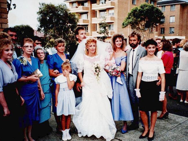 Undated images relating to the 2024 podcast - BRONWYN.  Missing mother Bronwyn Winfield with family members in 1990. From left:  Cousin Alison (surname unknown), Bronwyn's mother Barbara Read (holding gold purse), Bronwyn's grandmother Billie Hain, cousin Jayne Drewitt, Bronwyn's daughter Chrystal (front), Michelle Read (in bridal gown), Bronwyn's brother Andrew Read (groom, standing behind bride). Bronwyn Winfield (holding baby Lauren) is to the right of the bride. Next to Bronwyn is Jon Winfield, with his arm around his daughter Jodie.