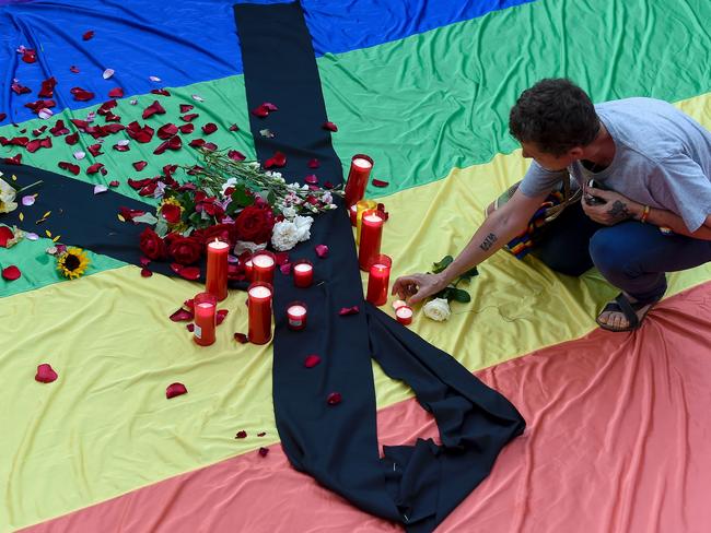 A mourner lights candles placed on rainbow flag draped with a black crepe outside Barcelona's city hall during a vigil at Sant Jaume Square in Barcelona. Picture: AFP