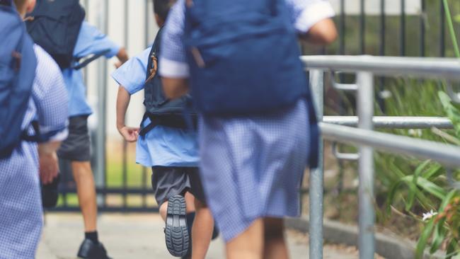 School children running away. They are wearing uniforms and carrying backpacks. They are having a race. Multi ethnic group with Asian, Caucasian and Aboriginal children. Rear view