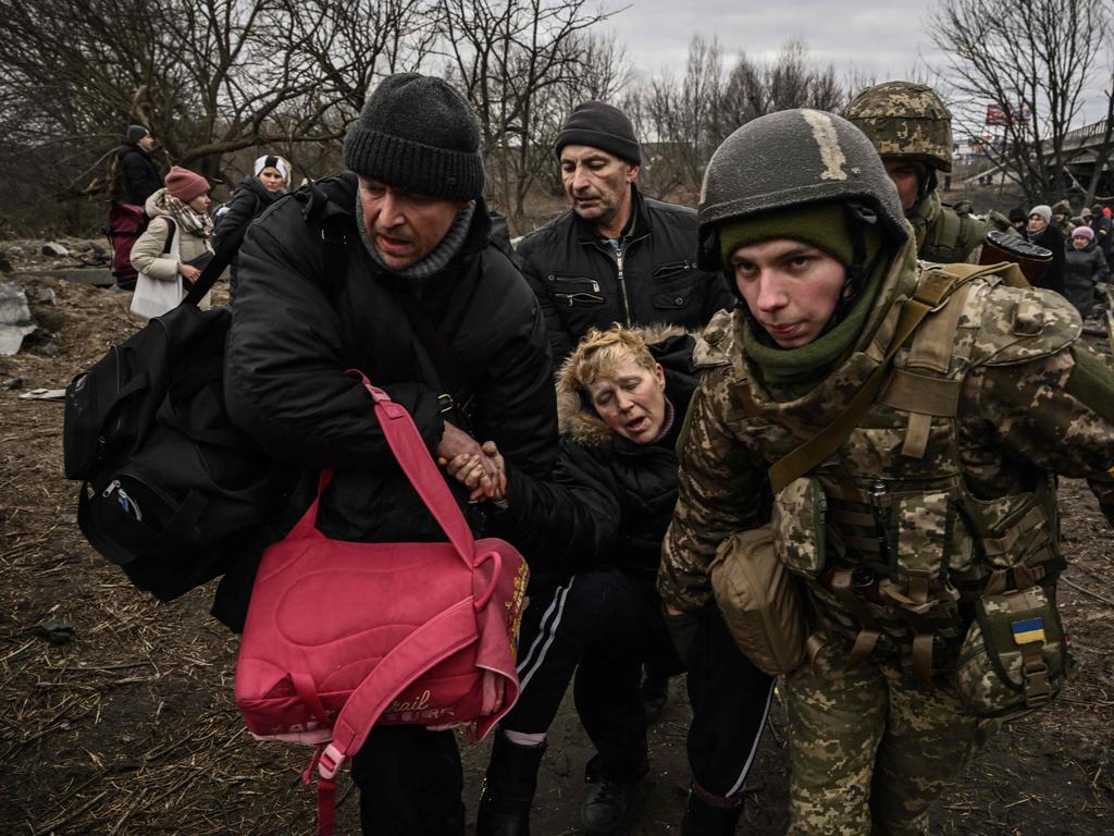 A woman is assisted while people cross under a destroyed bridge as they evacuate the city of Irpin, northwest of Kyiv, during heavy shelling and bombing on March 5, 2022. Picture: Aris Messinis / AFP.