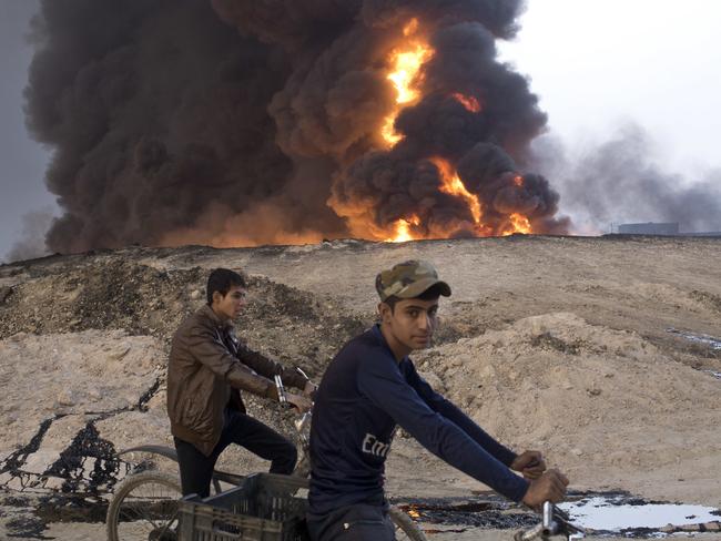 Youths ride bicycles next to a burning oil well in Qayyarah, about 50km south of Mosul.