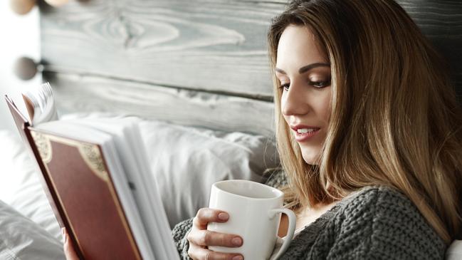 Woman drinking coffee and reading book on bedWellbeing from istock for Gold Coast Eye