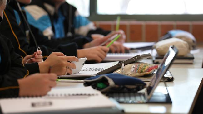 A student in uniform distracted holding using and watching a mobile phone during a lesson at high school.