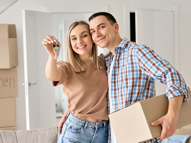 FIRST HOME BUYER Happy young couple home owners holding keys in new home. Smiling independent millennial man and woman first time homeowners carrying boxes on moving day. Mortgage loan, new house ownership concept.