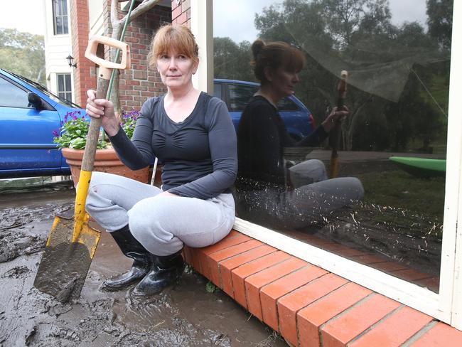 Chris Mackinnon takes a break after cleaning the front of her home at Paringa Parade, Old Noarlunga. The marks on the window show how high the water rose. Picture: Stephen Laffer