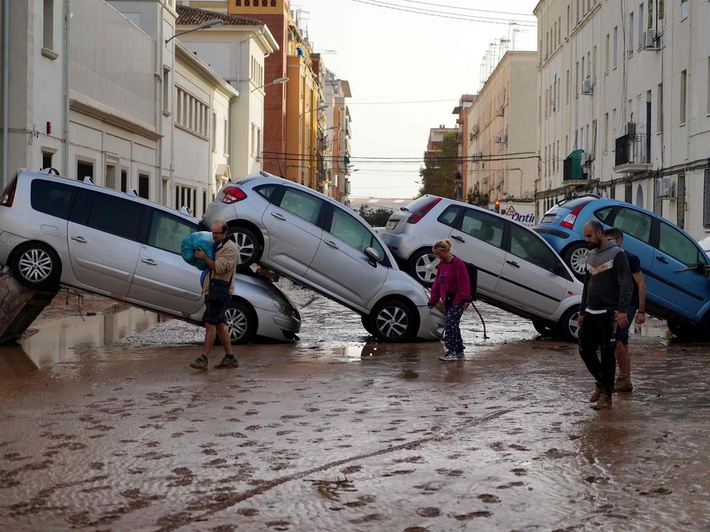 Residents walk past piled-up cars in Valencia’s De La Torre neighbourhood. Picture: Manaure Quintero/AFP