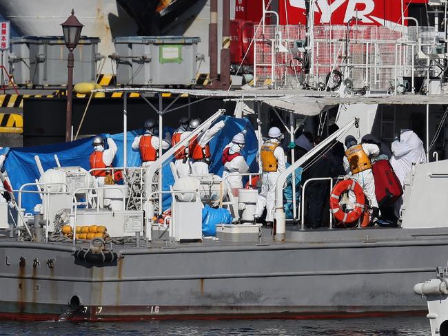 Workers in protective gear transfer a person under a blue sheet from the Diamond Princess cruise ship onto a Japan Coast Guard boat in Yokohama. Picture: AFP