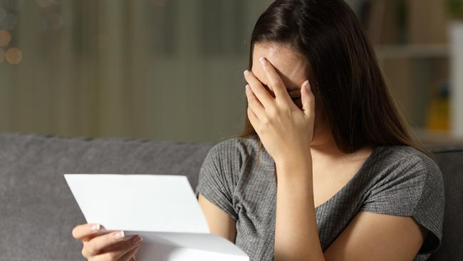 Sad woman reading a letter in the dark at home, renter, tenant, eviction, bill, stress, anxiety - for Herald Sun realestate