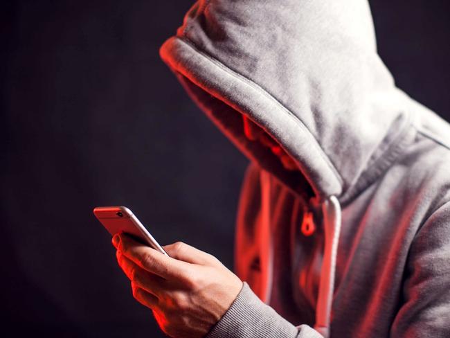 Man wearing hoody sweater with mobile phone in hands. Crime and hacking concept; scam generic.