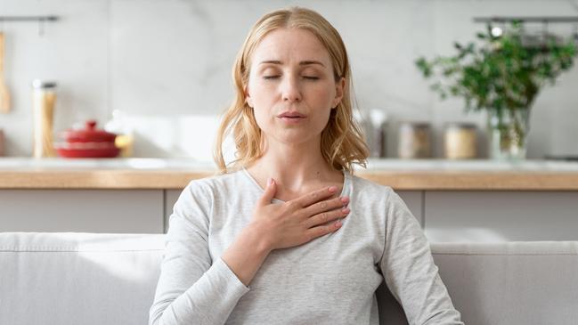 Concept of mental health. Woman sitting on couch and doing calming breathing exercises after panic attack. Female inhaling and exhaling to deep breath. Self-control, anxiety relief concept