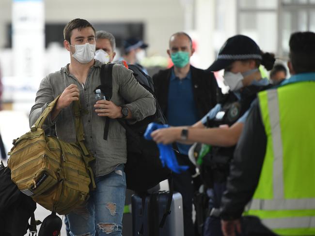 A member of the Defence Force watches over as returning overseas travellers are ushered towards waiting busses for the beginning of their 14-day imposed quarantine after arriving at Sydney International Airport in Sydney, Sunday, March 29, 2020. (AAP Image/Joel Carrett) NO ARCHIVING