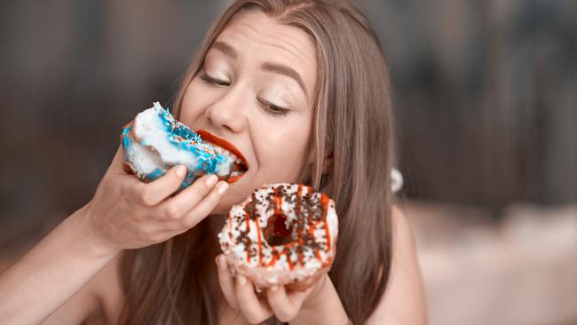 cute young woman holding donuts and biting it.cravinf for sweets.horizontal lifestyle shot. for Cairns Sun food column by Julia Wedding, June 6, 2017