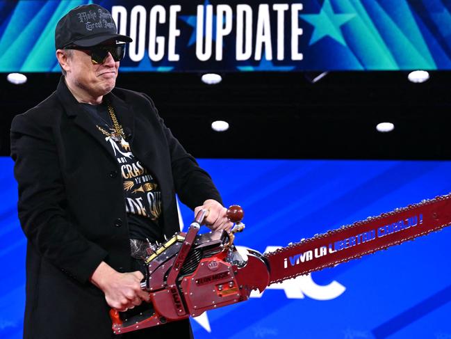 (FILES) Elon Musk holds a chainsaw reading 