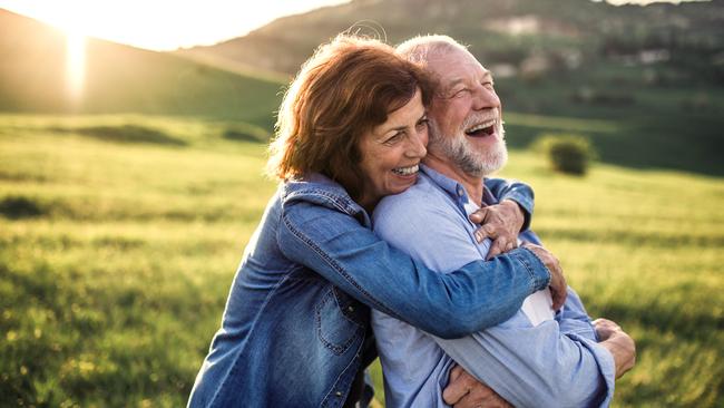 Happy senior couple outside in spring nature, hugging at sunset. Side view.