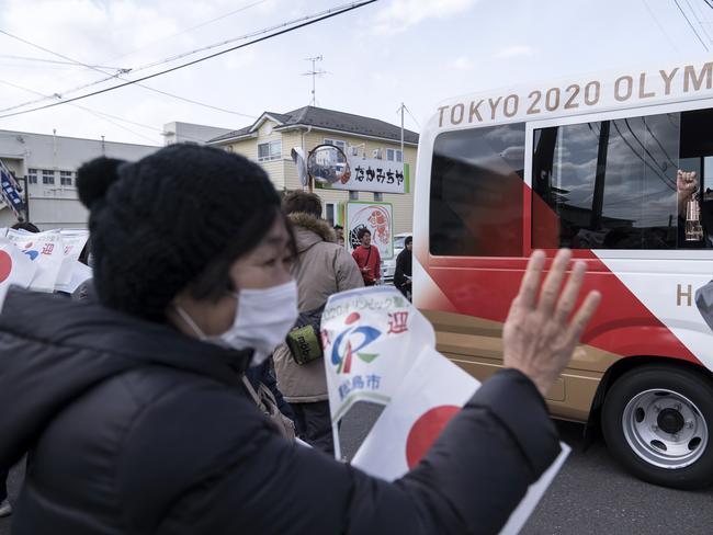 A woman waves to a bus transporting Japanese comedy duo Sandwich Man holding the Olympic flame after the Tokyo 2020 Olympic Games Torch Arrival Ceremony at the Japan Air Self-Defense Force Matsushima Air Base.