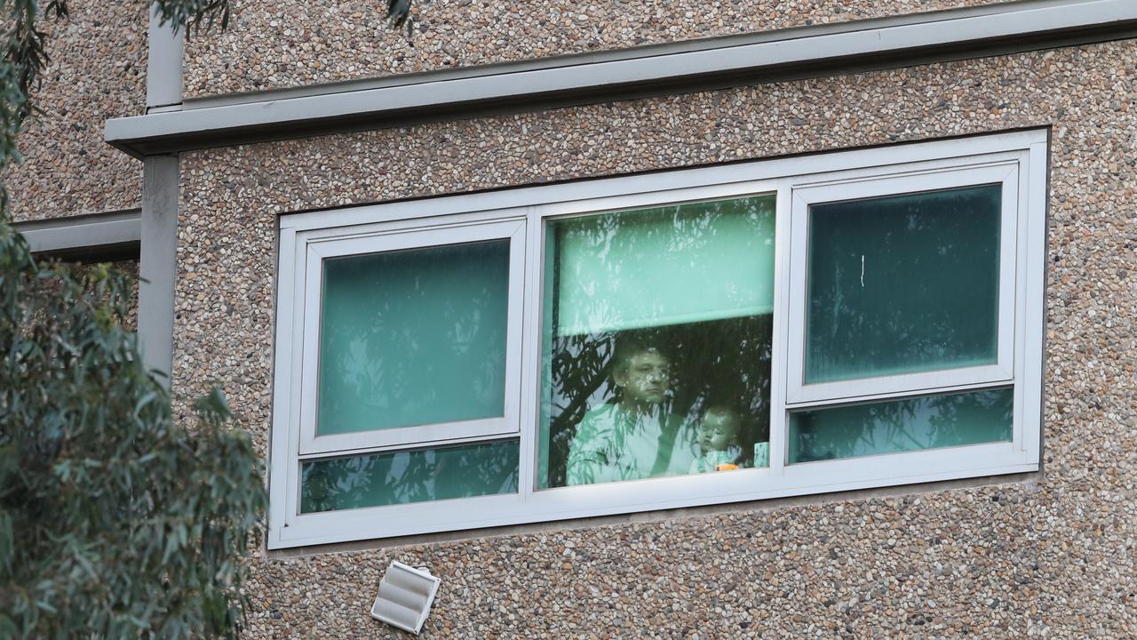 Residents peer out the windows at a large police presence at government housing building on Racecourse Rd in Flemington on Sunday morning. Picture: David Crosling