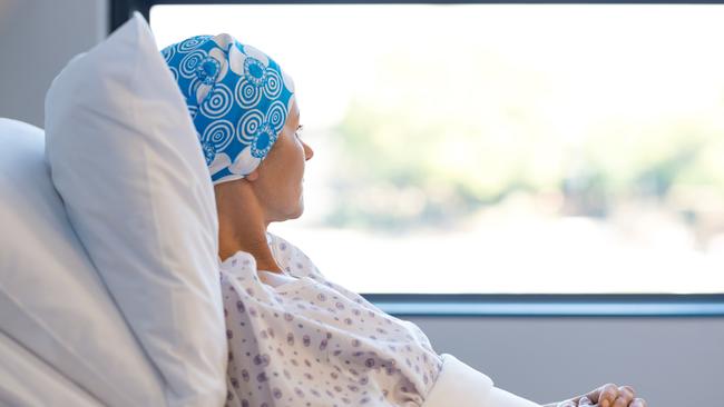 Young woman in bed suffering from cancer. Thoughtful woman battling with tumor looking out of window. Young patient with blue headscarf recovery in hospital on bed.