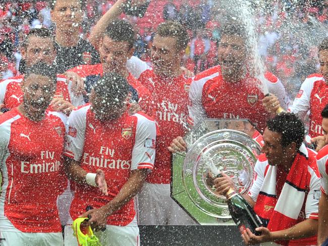 Arsenal players spray champaigne as they pose with the Community Shield trophy after Arsenal won the FA Community Shield football match between Arsenal and Manchester City at Wembley Stadium in north London on August 10, 2014. AFP PHOTO / GLYN KIRK -- NOT FOR MARKETING OR ADVERTISING USE / RESTRICTED TO EDITORIAL USE