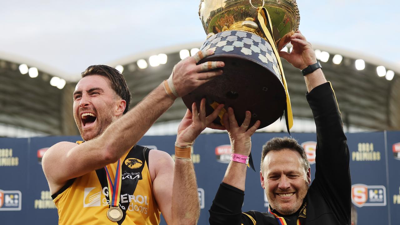 Glenelg coach Darren Reeves (right) lifts the 2024 Thomas Seymour Hill premiership trophy with captain Liam McBean after last season’s grand final triumph against Norwood. Picture: David Mariuz/SANFL