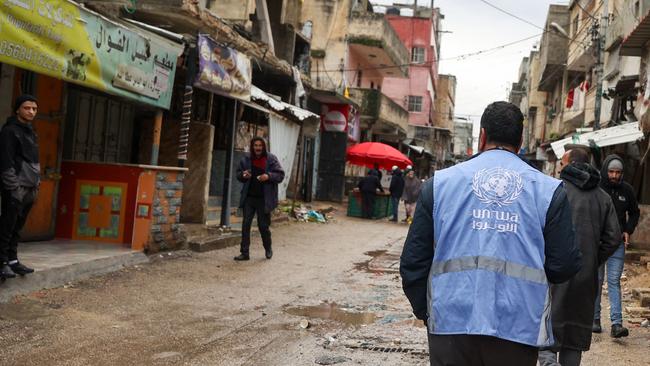 A man wearing a jacket bearing the logo of the United Nations Relief and Works Agency for Palestine Refugees (UNRWA), walks along a street in the West Bank.