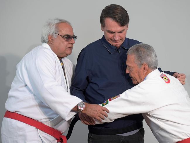 Brazilian far-right presidential candidate Jair Bolsonaro (C) receives an honorary black belt by Robson Gracie (L), son of the founder of the first Brazilian Jiu-Jitsu school, which was later turned into "Gracie Jiu-Jitsu", and Brazilian Jiu-Jitsu master Joa Carlos Austregesilo de Athayde (R) during a press conference in Rio de Janeiro, Brazil, on October 25, 2018. - The presidential runoff election takes place on October 28 in Brazil. (Photo by CARL DE SOUZA / AFP)